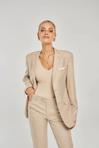 Glamour woman in stylish casual attire of pastel beige color posing with hand on waist on grey — Stock Photo