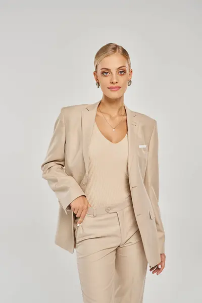 Attraente modella donna in total beige abbigliamento casual in piedi con mano sulla vita su grigio — Foto stock