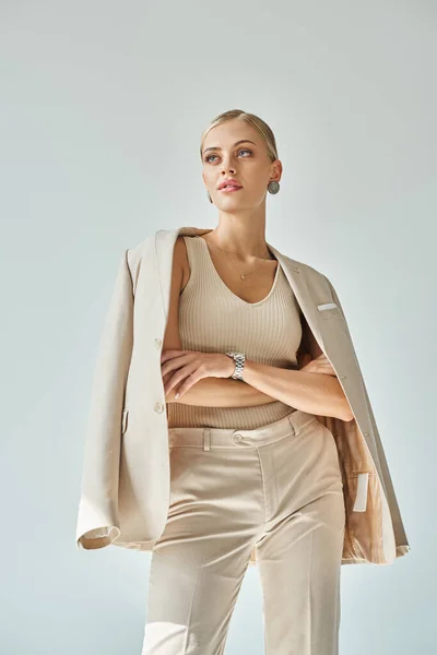Giovane donna bionda in total beige abbigliamento casual posa con le braccia incrociate e distogliendo lo sguardo sul grigio — Foto stock