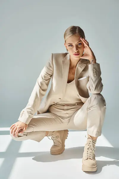 Femme élégante en vêtements beige et bottes lacées posant sur des hanches et regardant la caméra sur gris — Photo de stock