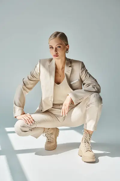 Modello di moda glamour in abito beige e stivali allacciati seduti sui fianchi al sole sul grigio — Foto stock