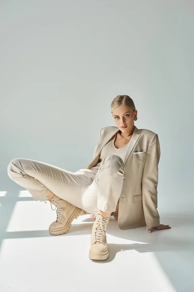 Sensual woman in pastel beige wear and laced boots posing and looking at camera in sunshine on grey — Stock Photo