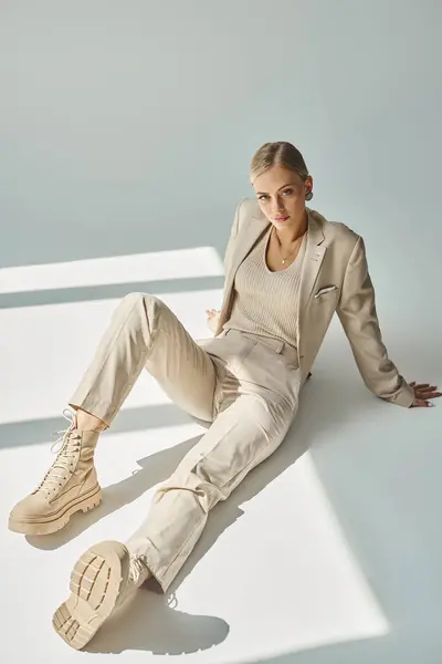Sensual woman in pastel clothes touching sitting in beige suit and laced boots in sunlight on grey — Stock Photo