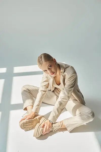 Зачаровує жінка в пастельному одязі, торкаючись шнурових черевиків, сидячи на сонці на сірому фоні — стокове фото