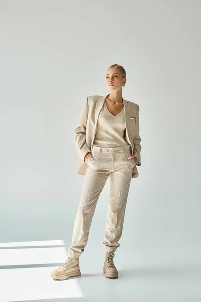 Donna alla moda in abito beige pastello posa con le mani in tasca e distogliendo lo sguardo sul grigio, a tutta lunghezza — Foto stock
