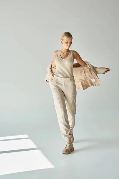 Charming woman in total beige outfit posing with stylish blazer on grey backdrop with sunlight — Stock Photo