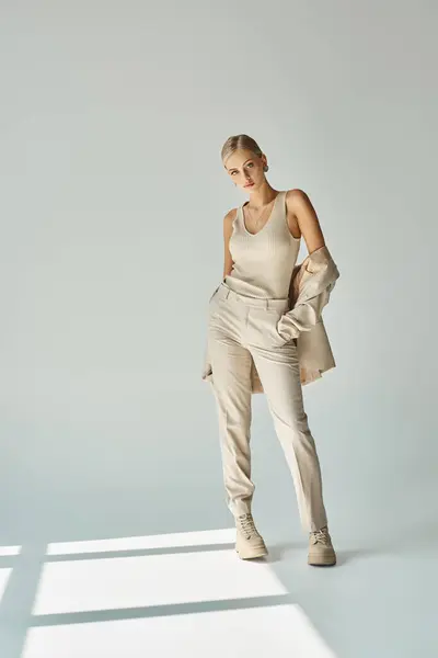 Young female model in beige tank top and pants holding blazer while standing on grey with sunlight — Stock Photo