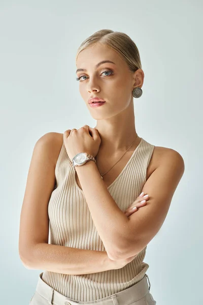 Портрет красивої блондинки в бежевому баку зверху і наручний годинник дивиться на камеру на сірому — стокове фото