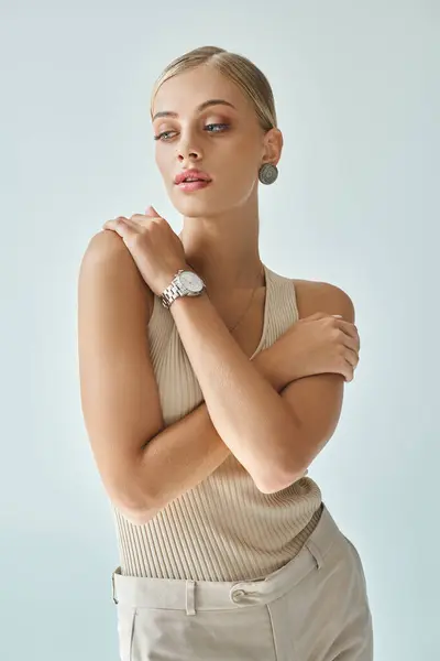 Séduisante femme en débardeur beige et montre-bracelet se câlinant sur le gris, la beauté et la mode — Photo de stock