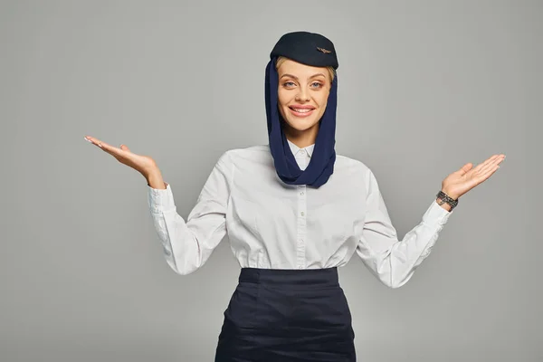 Fröhliche arabische Stewardess in Kopftuch und Uniform, die mit offenen Armen auf grau steht — Stockfoto