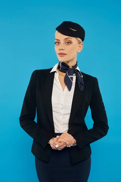Young attractive stewardess in elegant uniform looking at camera on grey backdrop, headshot — Stock Photo
