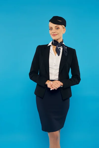 Hospedeira de bordo feminina em uniforme elegante sorrindo para a câmera enquanto está em pano de fundo cinza — Fotografia de Stock