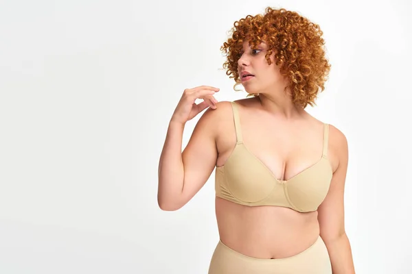 Plus size woman with red curly hair in bege underwear looking away on white, non-traditional beauty — Fotografia de Stock