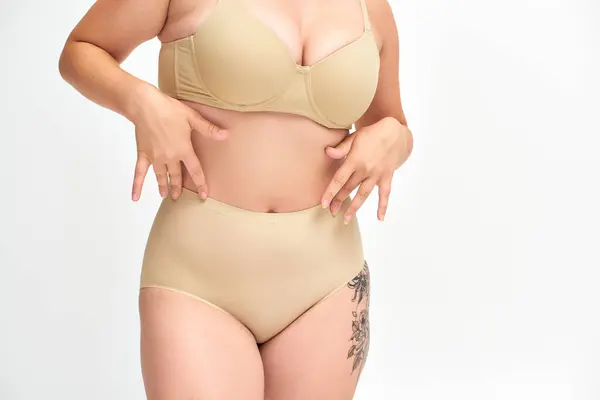 Vista ritagliata di giovane plus size donna in lingerie beige con anca tatuata su sfondo bianco — Foto stock
