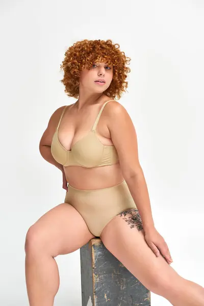 Femme captivante avec corps courbé posant en lingerie sur boîte en bois et regardant la caméra sur blanc — Photo de stock