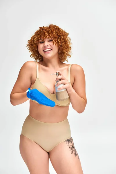 Happy redhead plus size woman in underwear with shower gel dispenser and bath glove on white — Stock Photo