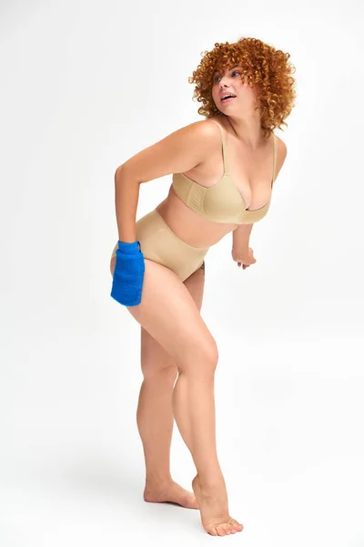 Full length of redhead plus size woman washing curvy body with bath glove on white — Stock Photo