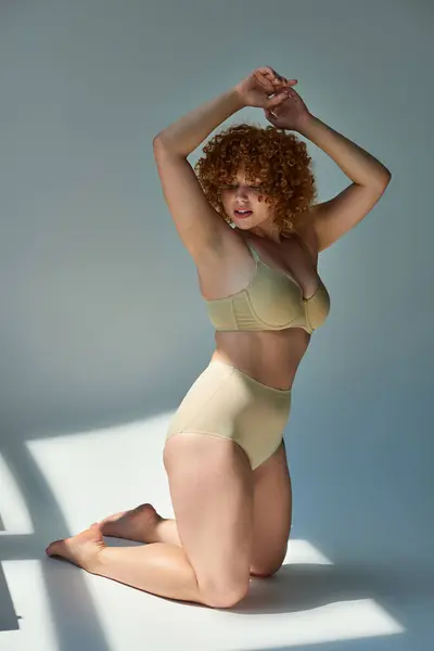 Redhead plus size model in taupe underwear in expressive pose in sunshine on grey backdrop — Stock Photo