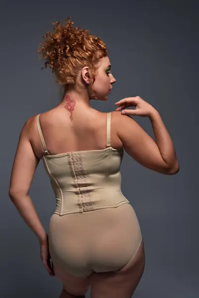 Vue arrière de rousse plus taille femme en sous-vêtements beige sur fond gris foncé, confiance en soi — Photo de stock