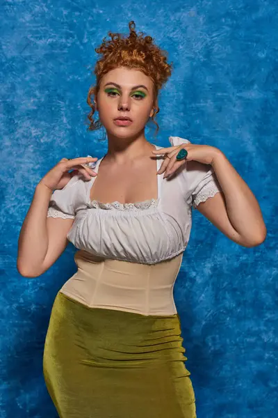 Stylish and redhead plus size woman in white blouse looking at camera on blue textured backdrop — Stock Photo