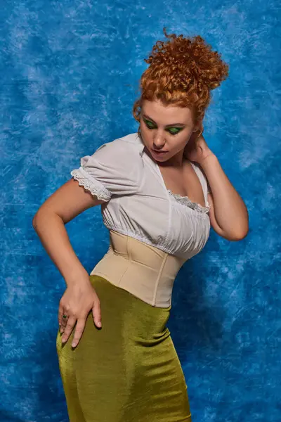 Jovem ruiva plus size modelo em traje elegante posando com a mão no quadril no fundo azul desigual — Fotografia de Stock