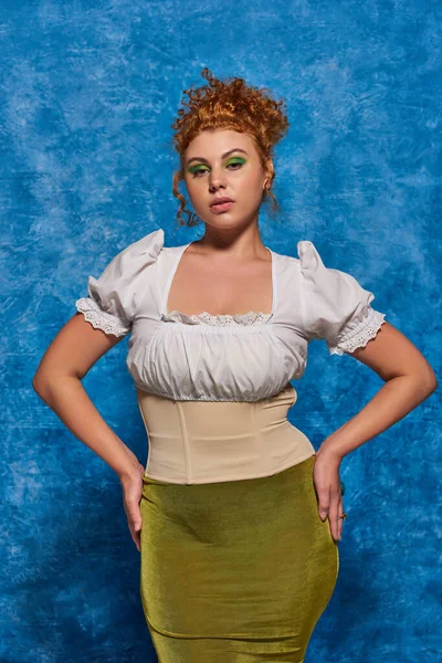 Charming redhead plus size model in elegant attire with hands on hips on blue textured backdrop — Stock Photo