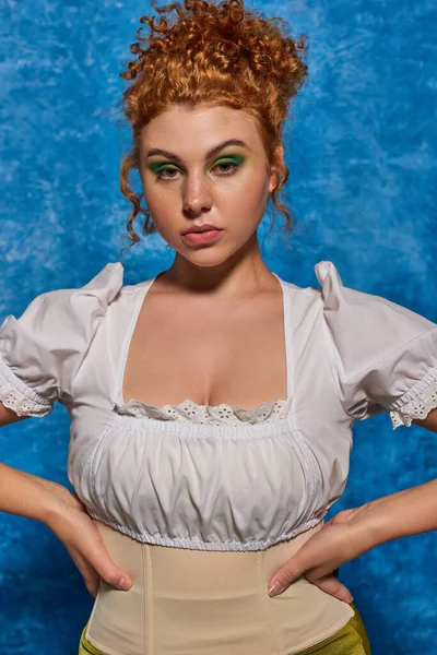 Beautiful redhead plus size model in trendy attire with hands on hips on blue textured backdrop — Stock Photo