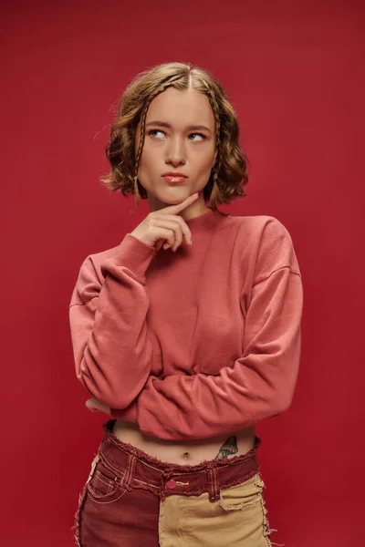 Pensive stylish and young woman in patchwork pants and cropped long sleeve posing on red backdrop — Stock Photo