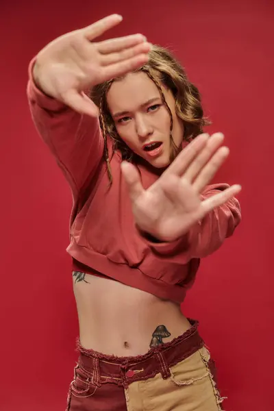 Самовираження, стильна молода жінка в обрізаному довгому рукаві, що показує жест рамки з руками на червоному — стокове фото