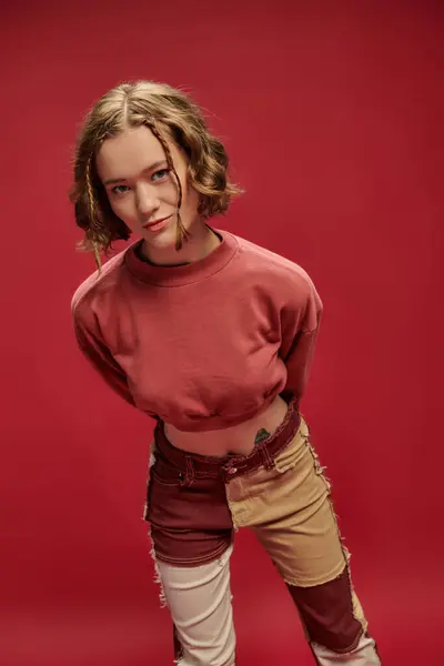 Personal style, young woman in patchwork pants and cropped long sleeve posing on red backdrop — Stock Photo