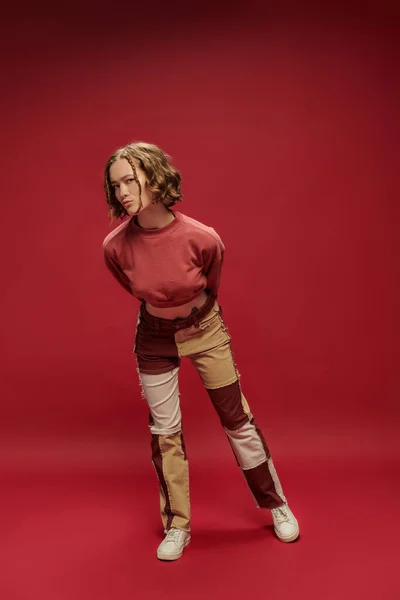 Personal style, young pretty girl in patchwork pants and cropped long sleeve posing on red backdrop — Stock Photo