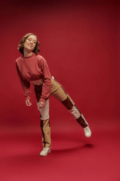 Persönlicher Stil, junges positives Mädchen in Patchworkhosen und abgeschnittenen Langarmpositionen, roter Hintergrund — Stockfoto