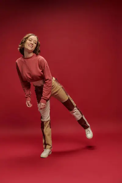 Personal style, young positive girl in patchwork pants and cropped long sleeve posing, red backdrop — Stock Photo