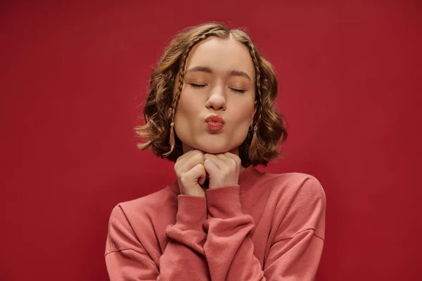 Portrait de jeune jolie femme aux cheveux courts ondulés et tresses boudant les lèvres sur rouge, air kiss — Photo de stock