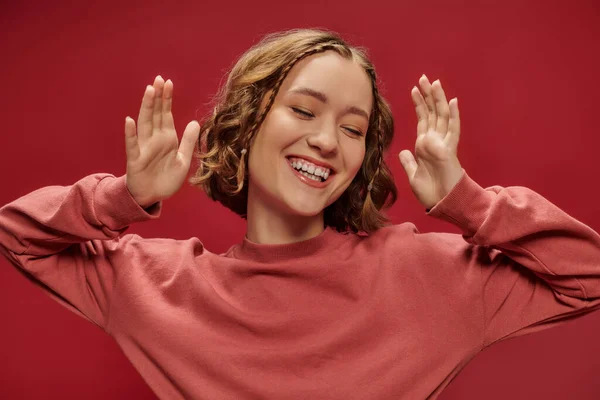 Emoción positiva, retrato de la joven mujer bonita con el pelo corto ondulado y trenzas sonriendo en rojo - foto de stock
