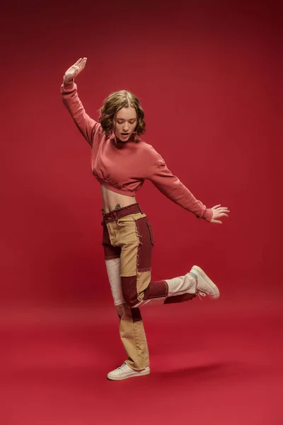 Stile personale, divertente gen z donna in pantaloni patchwork e ritagliato manica lunga gesticolando sul rosso — Foto stock