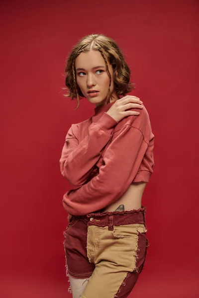Expresión personal, mujer sensual en pantalones patchwork y manga larga recortada abrazando hombro en rojo - foto de stock