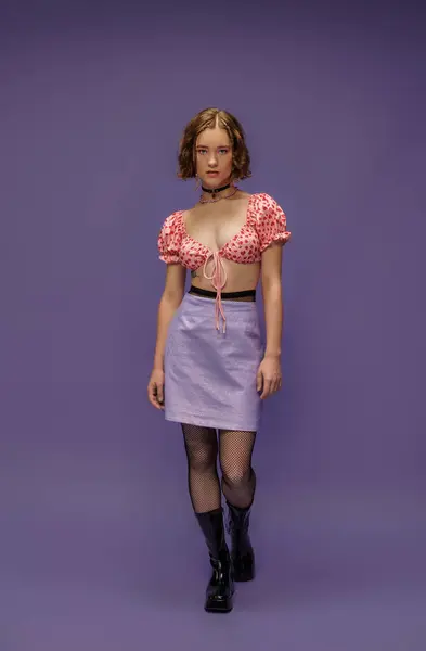 Pretty young woman in cropped top with heart shaped pattern and skirt standing on purple — Stock Photo