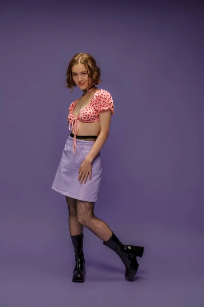 Smiling young woman in cropped top with heart shaped pattern and skirt standing on purple — Stock Photo