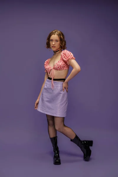 Mujer joven en la parte superior recortada con patrón de corazones y falda posando con la mano en la cadera en púrpura - foto de stock