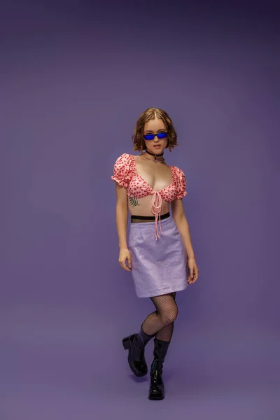 Pretty young woman in cropped top with hearts and skirt posing in sunglasses on purple — Stock Photo