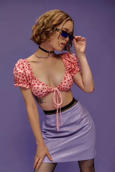 Mujer joven con estilo en traje de moda ajustando gafas de sol sobre fondo púrpura, estilo personal - foto de stock