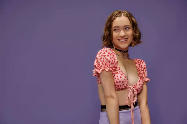 Glückliche junge Frau in abgeschnittenem Oberteil mit Herzen, die auf lila Hintergrund lächeln, positive Emotionen — Stockfoto
