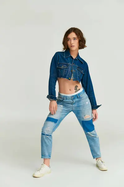 Self-expression, trendy young model in cropped denim jacket and blue jeans posing on grey background — Stock Photo