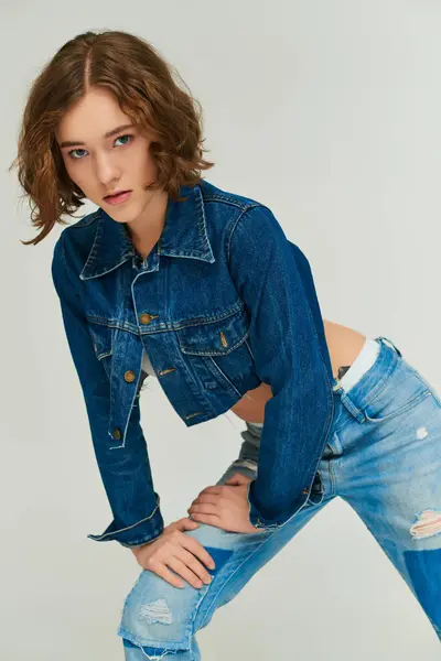 Self-expression, young model in trendy cropped denim jacket and blue jeans posing on grey background — Stock Photo