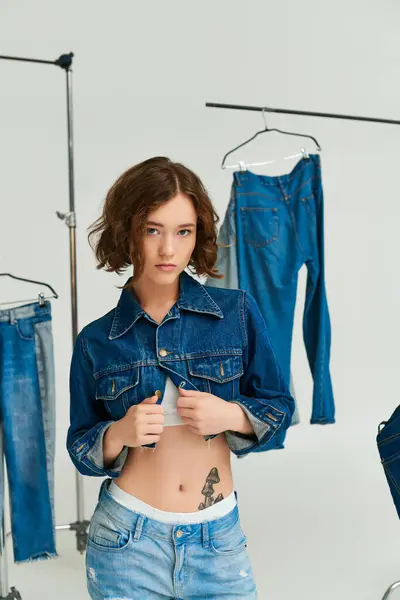 Gen z fashion, girl with tattoo posing in cropped blue jacket among denim clothes on grey backdrop — Stock Photo