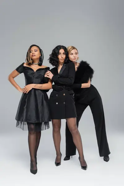 Vielfältige Gruppe modischer Freundinnen posiert in insgesamt schwarzer, eleganter Kleidung auf grau, voller Länge — Stockfoto