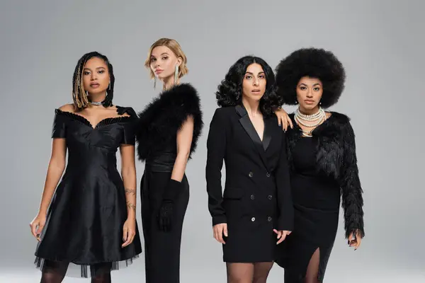 Multiethnische Damen in schwarzer eleganter Kleidung, die auf grauen, eleganten Freundinnen in die Kamera blicken — Stockfoto