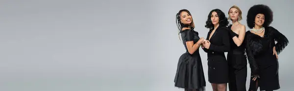 Mujer afroamericana feliz cogida de la mano de modelo elegante cerca de novias elegantes en gris, bandera - foto de stock