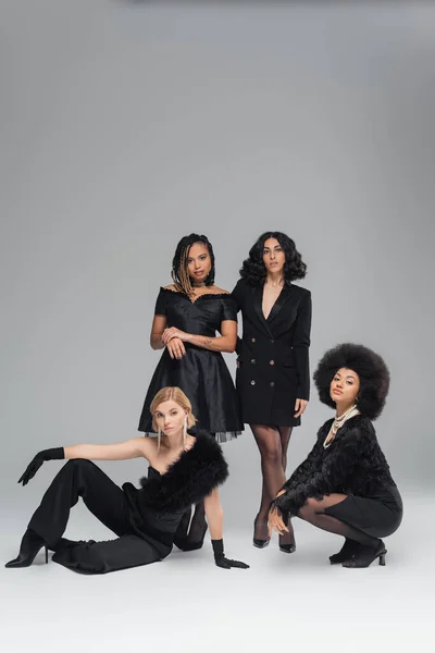 Group of diverse multiracial fashion models in black elegant outfits posing on grey backdrop — Stock Photo